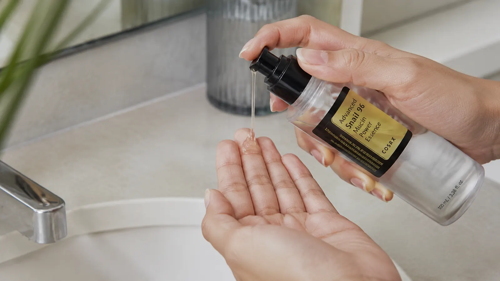 Hand dispensing clear gel serum from COSRX snail mucin bottle onto fingertips